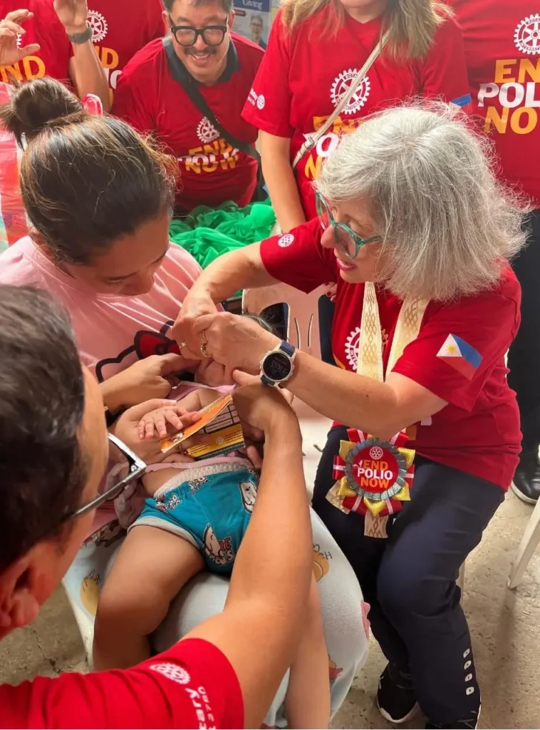 A Rotary volunteer in an End Polio Now shirt administers oral vaccine drops to a baby
